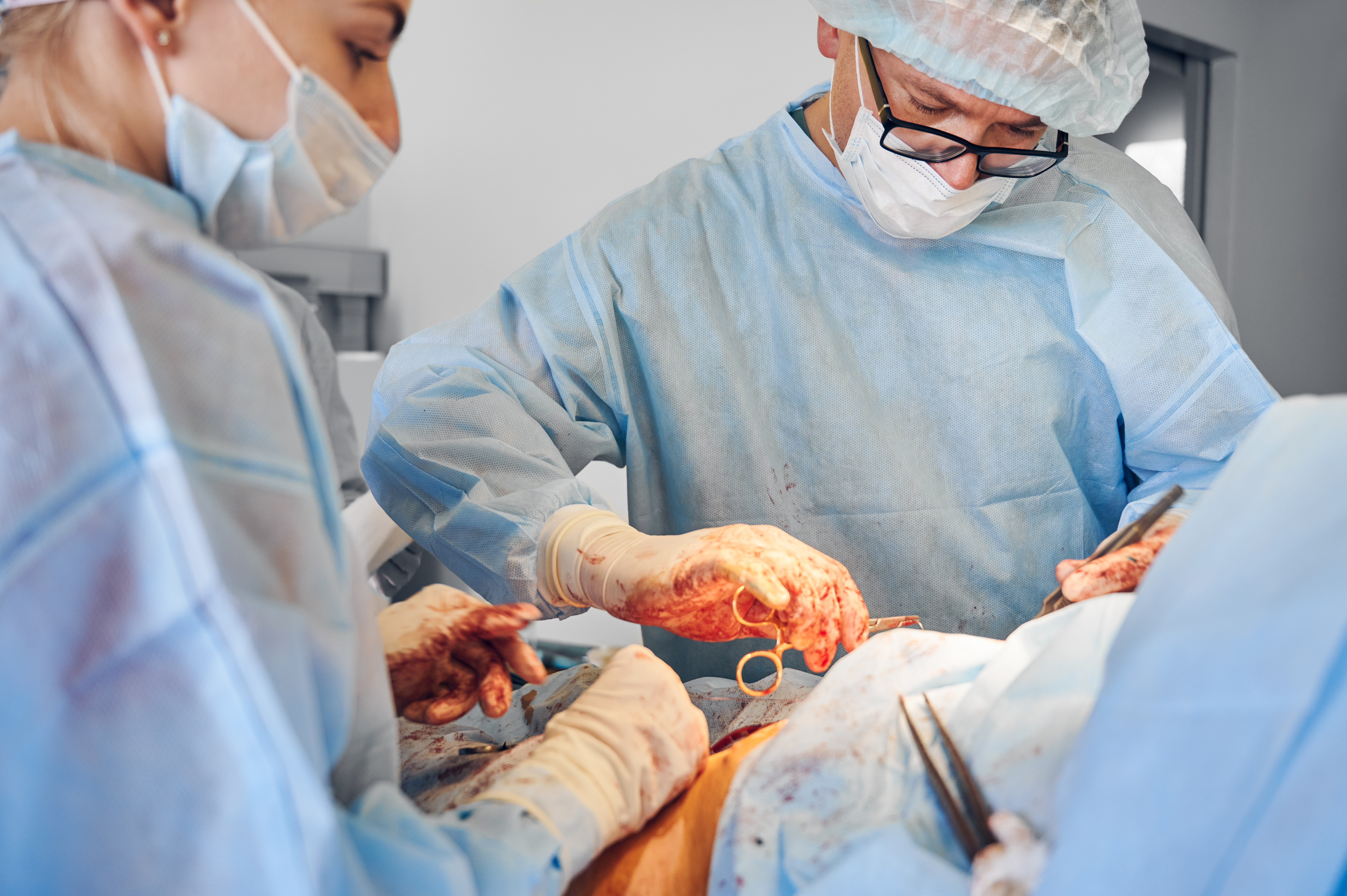 Doctors performing abdominoplasty or tummy tuck surgery in operating room. Male plastic surgeon and female assistant doing abdominal plastic surgery. Concept of medicine, tummy tuck, cosmetic surgery.